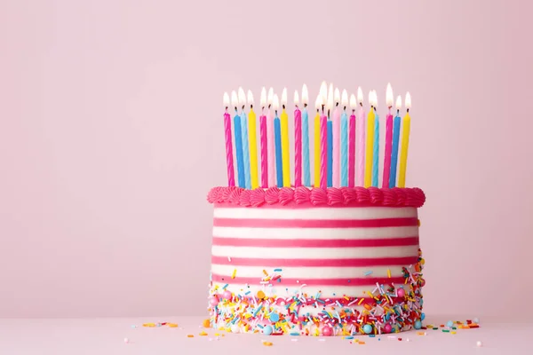 生日蛋糕 用粉色和白色条纹的奶油装饰 还有粉色背景下的许多生日蜡烛 — 图库照片