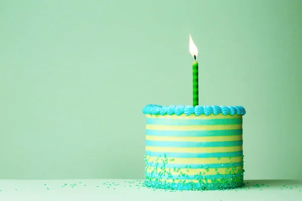 绿色和蓝色条纹生日蛋糕 有一个庆祝生日的蜡烛和一个普通的绿色背景 — 图库照片