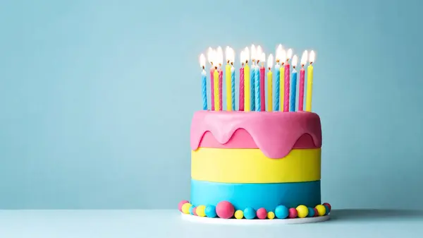 Bunte Geburtstagstorte Mit Vielen Geburtstagskerzen Und Tropfenglas Vor Blauem Hintergrund lizenzfreie Stockbilder