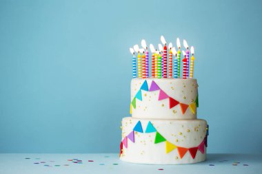 Renkli kutlama pastası ve mavi arka planda doğum günü mumları.