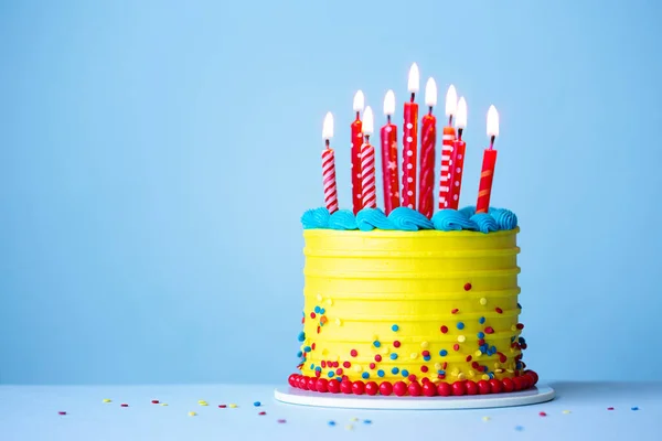 Colorful celebration birthday cake with yellow frosting and red birthday candles against a blue background