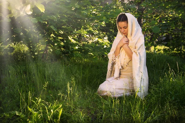 孤独な聖なる若い悲しい東ユダヤメアリー古いレトロなショールベール布公園芝生の芝生の膝の手に座る願い主イエス キリストを求めると思う 農村部の女性幸せな喜びの顔天使を請う賛美の信頼平和太陽の光 — ストック写真