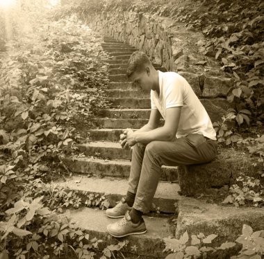 Genç yaşta ruhsal çöküntüye uğramış kederli çocuk umut dolu seyahat koltuğu eski model vintag şehir tuğlası harabe çalgı alanı yorgun insan tipi bekle Tanrı 'ya inan eski köy evinin duvarına ibadet et