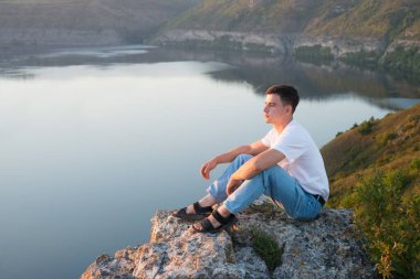 Kırsal, yalnız, üzgün, kendini Tanrı 'ya adamış genç bir adam. İsa Mesih' in inancı. Hayata güven. Neşeli, neşeli, inançlı, duacı çocuk sakin, vahşi park ağacı göleti vadisi manzarasına bak.