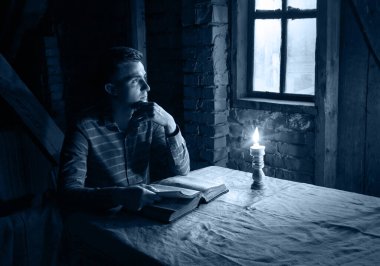 Genç yalnız başına umut dolu insan yüzü kutsal ilahi İsa koltuğu bak ve kutsal sayfayı aç. Antika İsrailli üzgün, yalnız, erkek çocuk. Koyu siyah, alev ışıklı, masa başı, kilise odası.