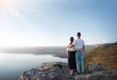 2 genç taşralı erkek, neşe dolu bir eğlence istirahatı için güneşli bir ortama bakıyor. Mutlu bir gülümseme, bayan partner yürüyüşçüsü, el ele tutuşun barış yürüyüşü yapın, uçurumun zirvesine tırmanın.