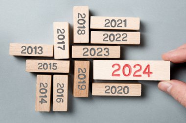 Gri sayılı tahta blokların fotoğrafı ve bir tanesi tahta yüzeyine 2024 numaralı kırmızı damgalı bir insan elinin yanında duruyor. Gri Arkaplan. Yeni Yıl, İş Stratejisi, İnovasyon ve Dikkate Alınan Konsept.