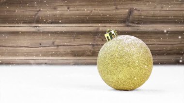 Karda tek bir altın topun karla kaplı olduğu sakin bir hayat. Arka planda ahşap masa. Düşen kar etkisi. Noel, tatil ve kış konsepti. Yüksek kalite 4k video.