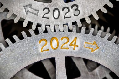 2024 ve 2023 numaralı diş tekeri mekanizmasının fotoğrafı ve metal yüzeyine kazınmış oklar. Yeni yıl konsepti.