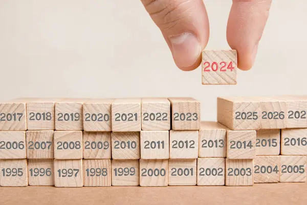 木製のブロックの写真は灰色の数字で そのうちの1つは木製の表面に刻まれた赤い番号2024の人間の手で保持しています 新年コンセプト ロイヤリティフリーのストック画像