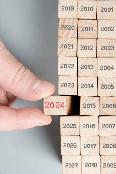 木製のブロック列の写真は灰色の数字で そのうちの1つは木製の表面に刻まれた赤い番号2024の人間の手で保持しています グレイ バックゴンド 新年コンセプト ロイヤリティフリーのストック写真