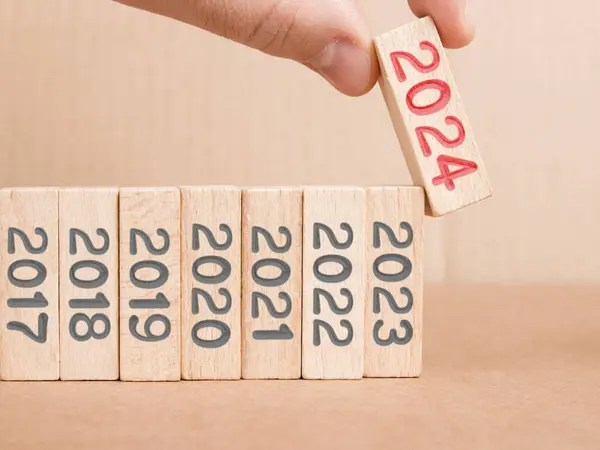 照片上有一排灰色数字的木制方块 其中一个方块由一只红色数字2024印在木制表面的人类手拿着 新年概念 图库照片