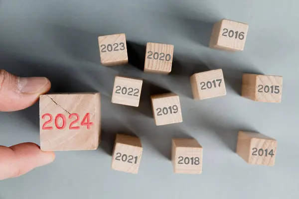 木製のブロックグループの写真は 何年も経過した灰色の数で そのうちの1つは 木製の表面に刻まれた赤い番号2024を有する人間の手で保持しています そしてスタンディングアウトコンセプト ストックフォト