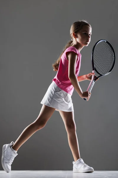 ピンクの衣装を着た若い女性テニス選手 ラケットとボールでポーズをとる少女 ハーフサイドライトシルエットを背景にグレー — ストック写真