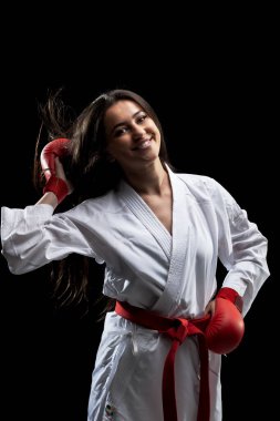 Güzel, mutlu bir kız. Siyah arka planda karate kıyafeti, kimono ve kırmızı eldivenlerle poz veriyor ve gülümsüyor.