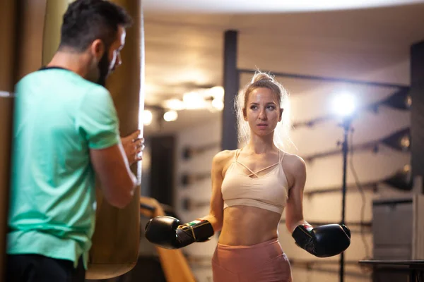 ボクシングの手袋で女の子をフィット フィットネススタジオでバッグをパンチとキックボックスを練習女性クライアントと男性フィットネスインストラクター — ストック写真
