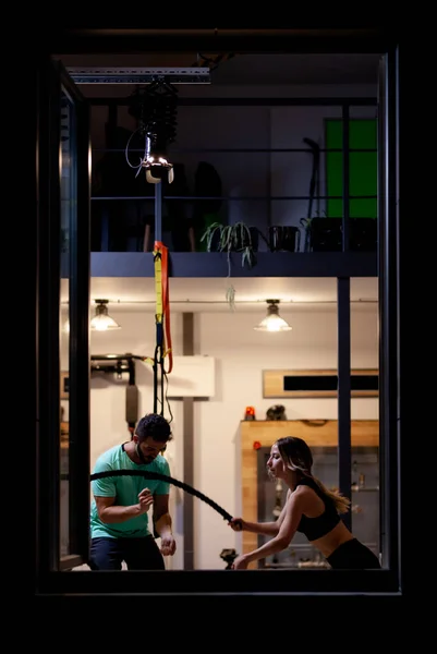在健身室用绳子和男健身教练一起锻炼的女孩 从窗外看 — 图库照片