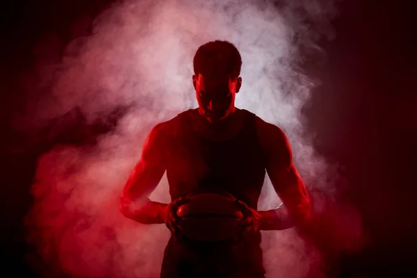 篮球队队员一边闪烁着红色的光芒 一边拿着一个烟雾弥漫的背景球 严重集中的非洲裔美国人 — 图库照片
