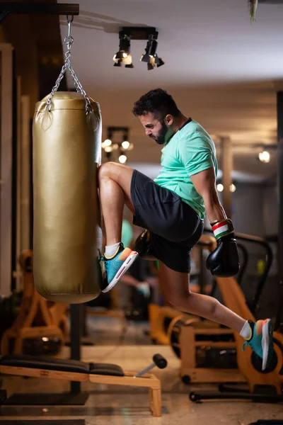 筋肉男ともにボクシング手袋ジャンプヒットAパンチングバッグで膝でフィットネススタジオ — ストック写真