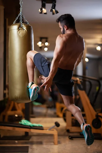 Muscular Shirless Mężczyzna Skok Uderzając Worek Bokserski Kolanem Studio Fitness — Zdjęcie stockowe
