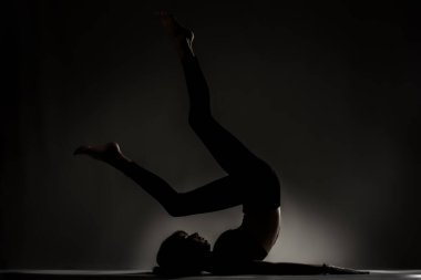 Fit balerin kız yalan söylüyor ve yoga pozları veriyor. Koyu arkaplana karşı yan aydınlatma silueti.