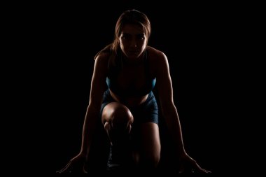 Female runner in low race start position. Girl in sportswear against dark background