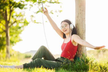 Koyu saçlı kız akıllı telefonundan kulaklıkla müzik dinliyor.