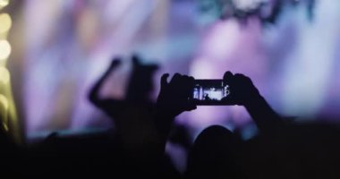 Kalabalığın içindeki soyut siluet insanlar ellerini kaldırıp dans ediyorlar ve ellerinde akıllı telefonlar tutuyorlar. Işık yanıp sönüyor ve odak noktasını kaybediyor