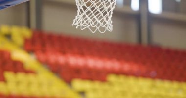 Antrenman sırasında ağlı basketbol potası. Sayı yapan iki top. Arka planda renkli sandalyeler.
