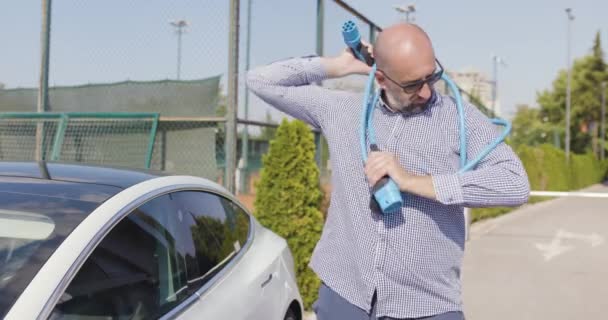 電気自動車の充電ケーブルに問題があるひげとサングラスを持つ大胆な男 — ストック動画
