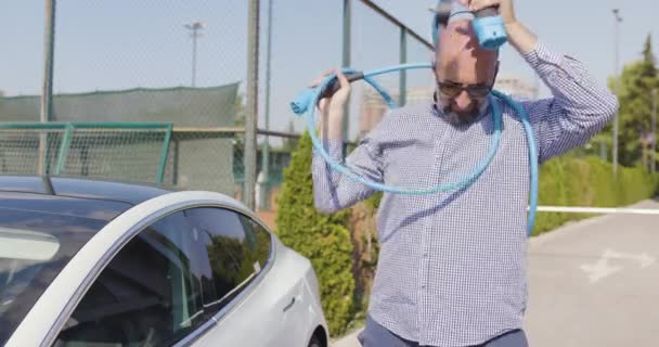 ひげとサングラスを持つ大胆な男は電気自動車の充電ケーブルに問題がある — ストック動画