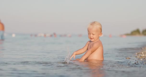 小女孩坐在浅水的海滩上 浪花和水花 — 图库视频影像