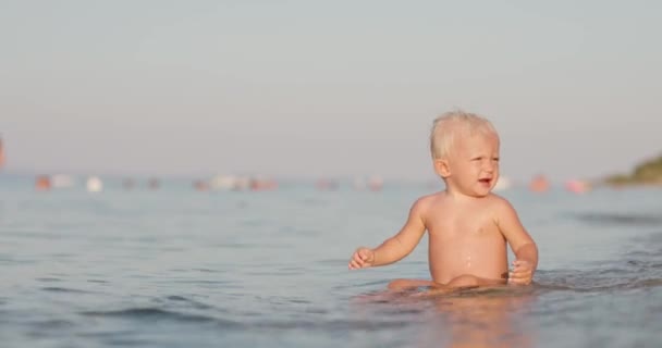 赤ちゃんの女の子は浅い水の中でビーチに座って泣いて — ストック動画