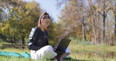 Çayırda otururken dizüstü bilgisayarda çalışan güzel bir kız. Parkta şık bir genç bayan. Sağ kamera hareketi.