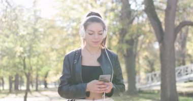 Kulaklıklı güzel bir kız telefona bakıyor. Parkta yürüyen şık genç bir bayan. El bilgisayarı videosu.