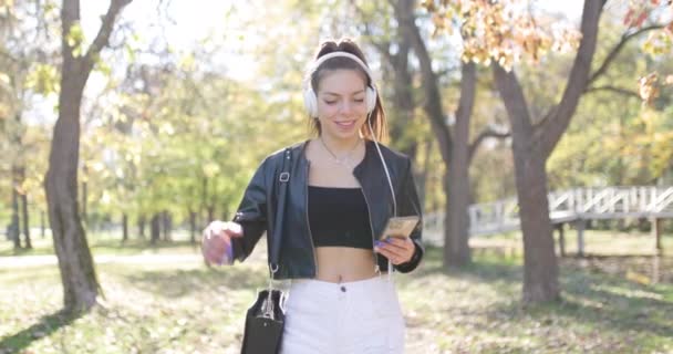 Kulaklıklı Güzel Bir Kız Telefona Bakıyor Parkta Yürüyen Şık Genç — Stok video