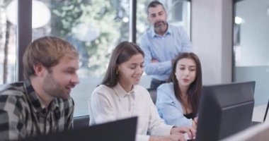 Ofiste çalışan genç iş arkadaşları. Kıdemli amir ayakta duruyor ve tavsiye veriyor. Başarılı ekip bir sorunu çözüyor.