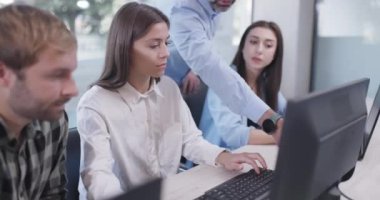 Ofiste çalışan genç iş arkadaşları. Kıdemli amir ayakta duruyor ve tavsiye veriyor. Başarılı ekip bir sorunu çözüyor.