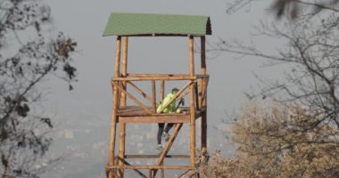 Dağlardaki ahşap gözetleme kulesine tırmanan bir adam şehir manzaralı. Trail runner hedefine ulaşıyor. Ara veriyoruz..