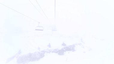 Six person chairlift on steel cable moving in clouds. Foggy weather in ski resort. Speed up video.