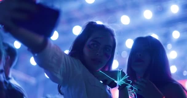 2人のシルエットの女の子は多くのライトで大きなステージの前で携帯電話でセルフィー写真を撮る — ストック動画