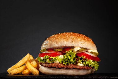 Soğanlı hamburger, salatalık, salatalık, patates kızartması ve koyu gri arka plan..