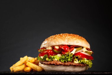 Soğanlı pastırmalı hamburger, salatalık, salatalık ve patates kızartması, koyu gri arka planda..