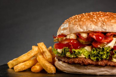 Soğanlı pastırmalı hamburger, salatalık, salatalık ve patates kızartması, koyu gri arka planda..