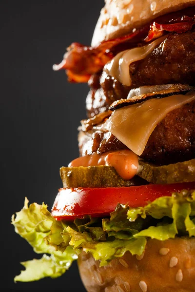 Abstract double burger with bacon cheese onions tomatoes cucumber and lettuce. Against dark background.
