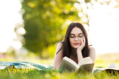 Parkta elinde kitapla yatan güzel bir kız. Güneşli bir yaz gününde açık hava aktivitesi.