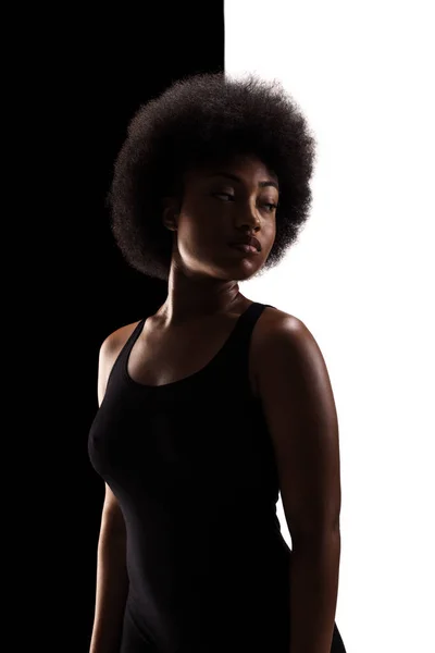 Half silhouette studio portrait of african american girl with curly hair afro hairstyle against black and white background.