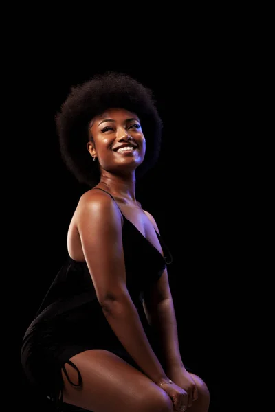 Studio portrait of elegant african american lady with curly hair afro hairstyle against black background. Happy girl smiling in black dress.