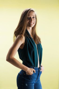 Sarı arka planda güzel bir kız. Süslü gömlekli ve kot pantolonlu esmer kadın stüdyoda poz veriyor..