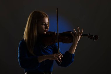 Beautiful blond girl playing violin. Female violinist against dark blue background.